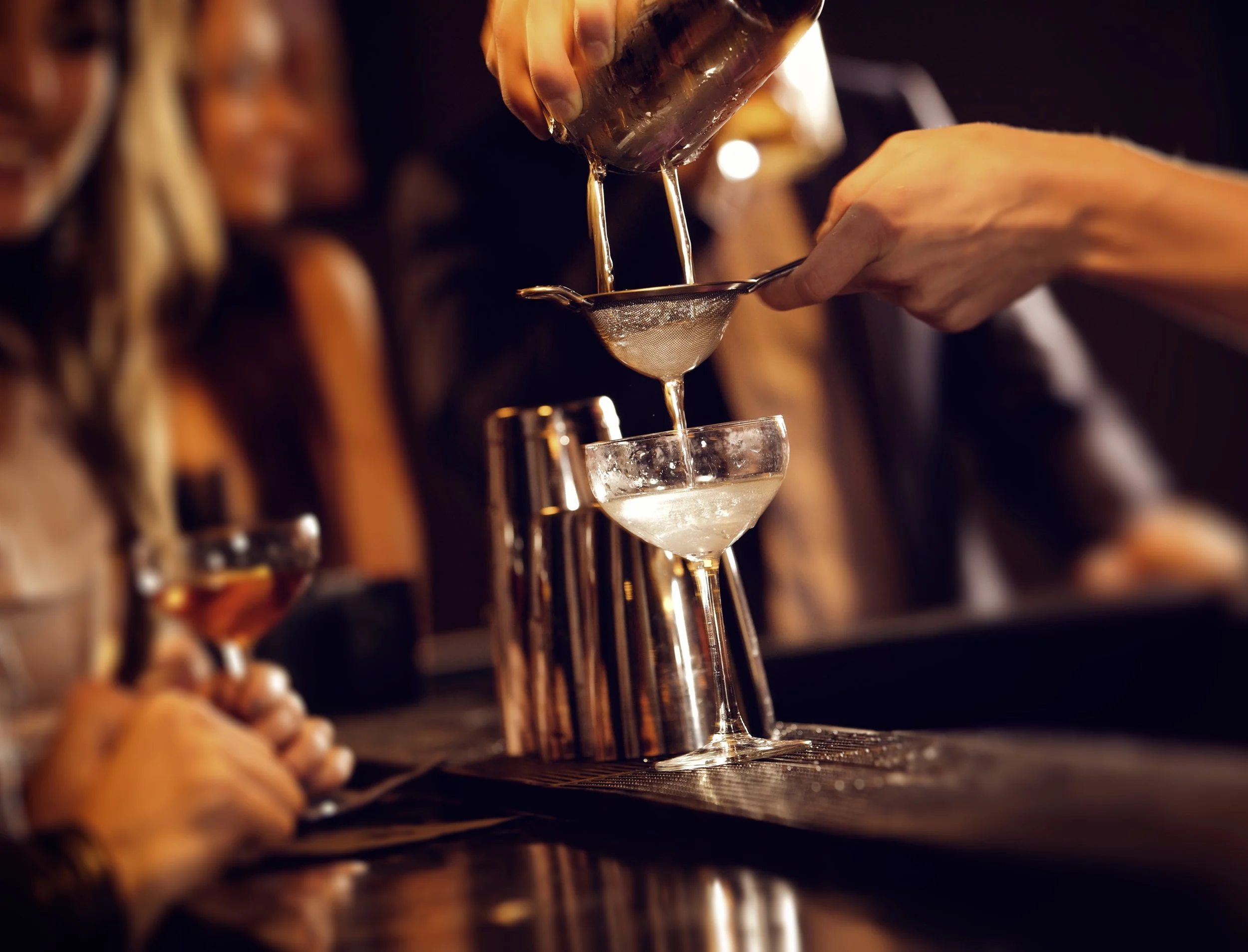Bartender straining a cocktail into a coupe glass